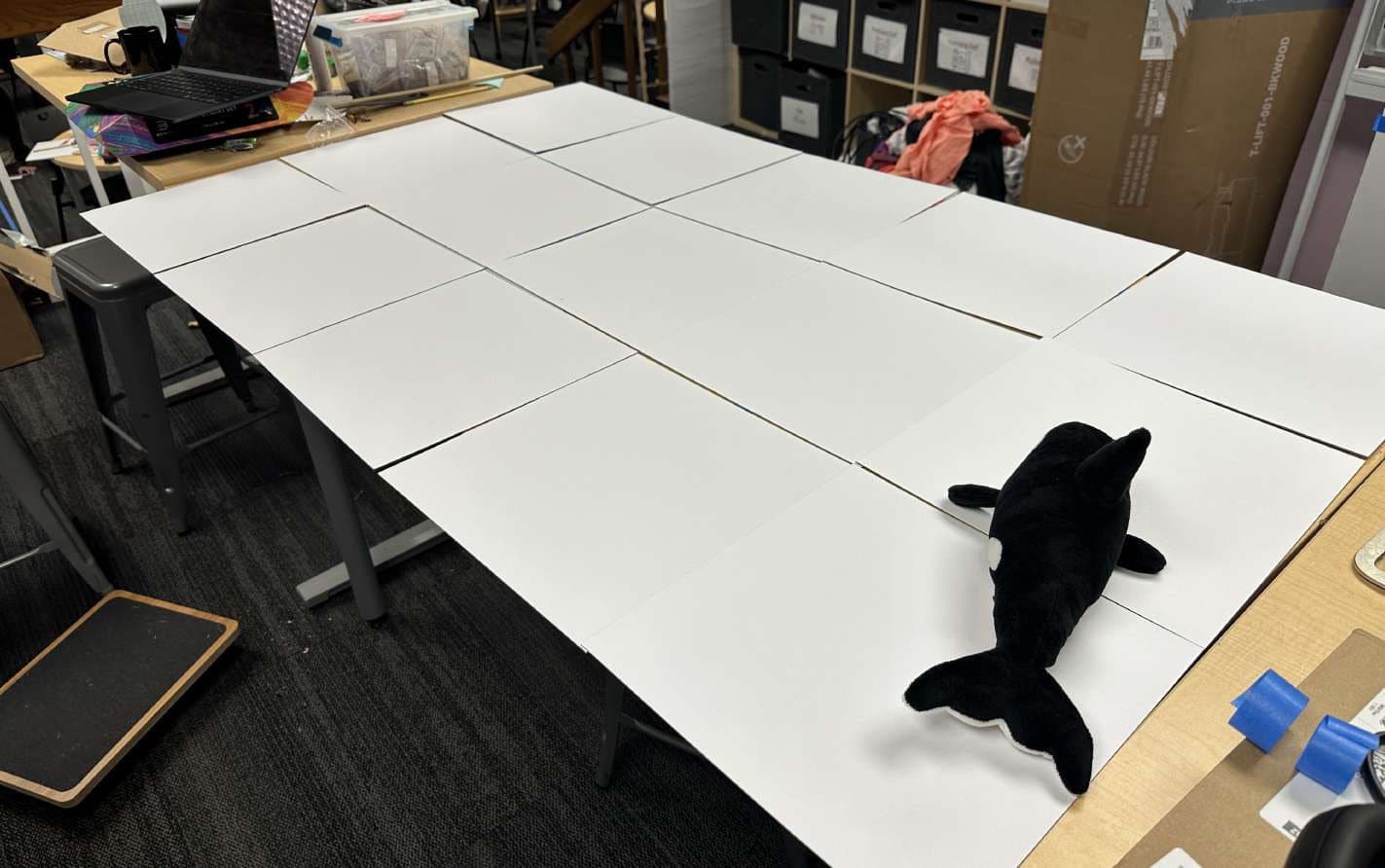 Paper grid on a table with an orca plush marking a cell