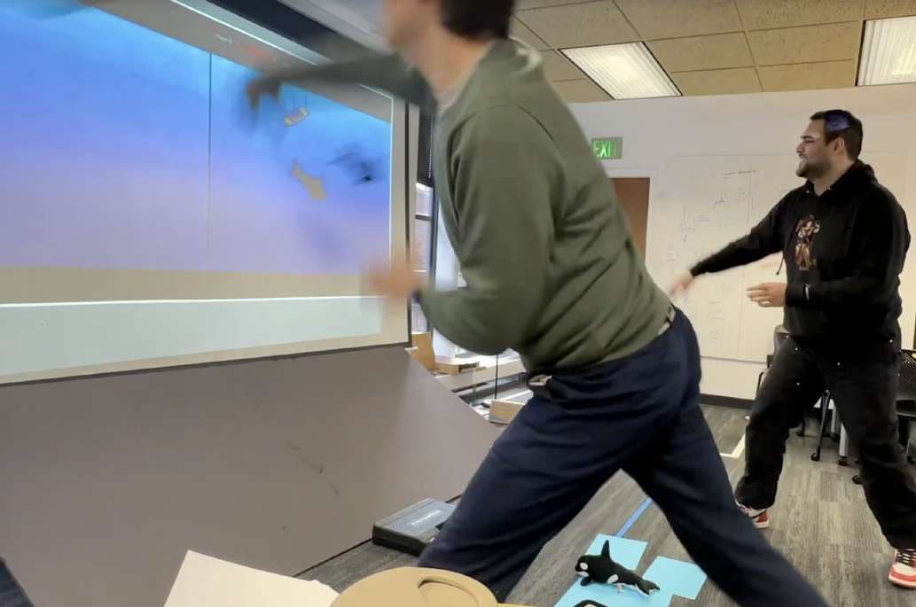 Person throwing an orca plushie at a projected screen